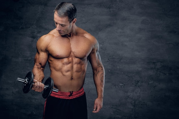 Portrait of athletic, muscular shirtless middle age male holds dumbbell.