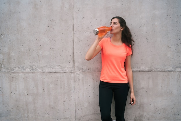 Portrait of an athletic woman drinking water after training against grey background. Sport and health lifestyle.