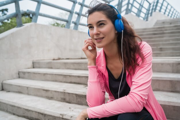 階段に座ってトレーニングの休憩中に音楽を聴いている運動女性の肖像画。スポーツと健康のライフスタイルの概念。