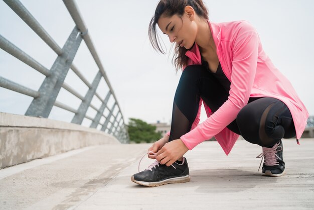 Portrait of an athletic woman  tying her shoelaces and getting ready for jogging outdoors. Sport and healthy lifestyle concept.