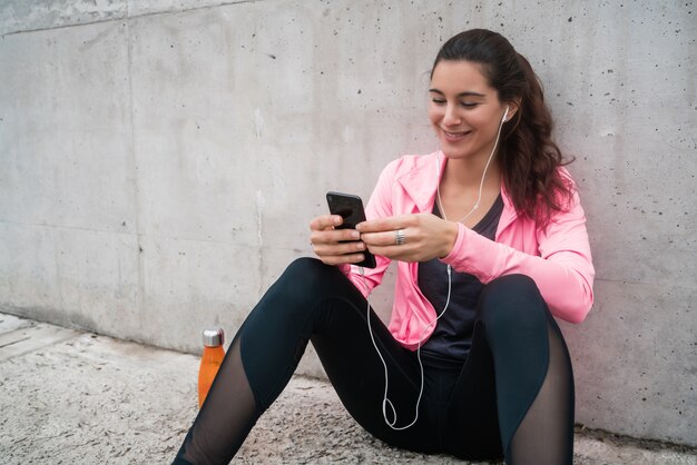 灰色の背景に対してトレーニングの休憩中に彼女の携帯電話を使用して運動する女性の肖像画。スポーツと健康のライフスタイル。