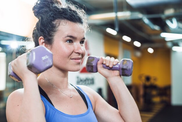 Портрет спортивной молодой женщины, делающей упражнение с гантелями