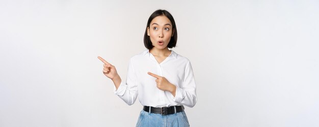 Portrait of attractive adult asian woman pointing looking left with pleased smile showing banner or