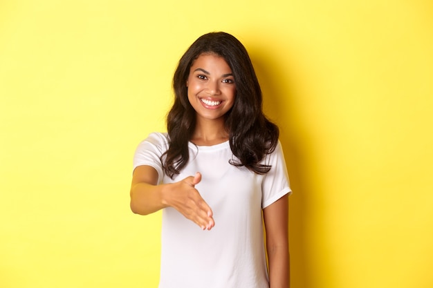 Ritratto di una ragazza afroamericana attraente che sorride allungando la mano per il saluto della stretta di mano