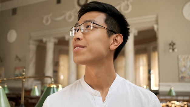 Портрет привлекательного азиатского студента в очках, обучающегося в университетской библиотеке
