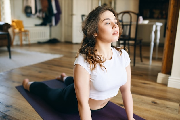 Free photo portrait of attractive barefooted young female with curvy body exercising at home in sportwear, stretching body, doing upward facing dog pose, opening shoulders and chest, bending her back