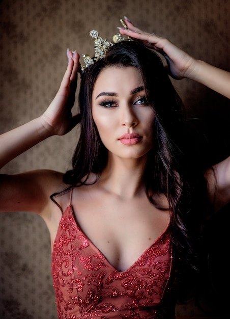 Free photo portrait of an attractive beautiful brunette girl dressed in red dress with make-up in the precious crown