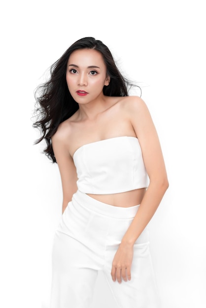 彼女は白い背景に白いドレスを着て化粧品の健康的な外観でポーズをとってファッションの魅力的な美しさのアジアの女性の肖像画