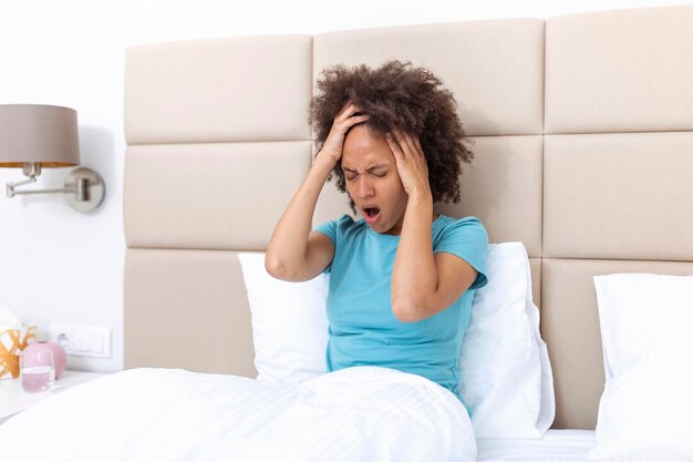 Портрет привлекательной чернокожей женщины в постели дома с головной болью, чувством боли и выражением нездоровья