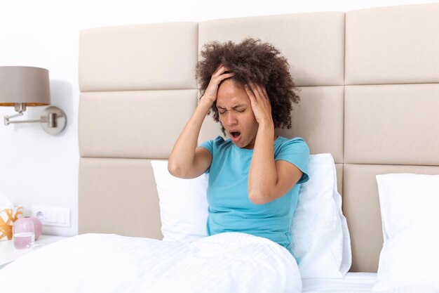 Portrait of an attractive black woman in bed at home with a headache feeling pain and with an expression of being unwell