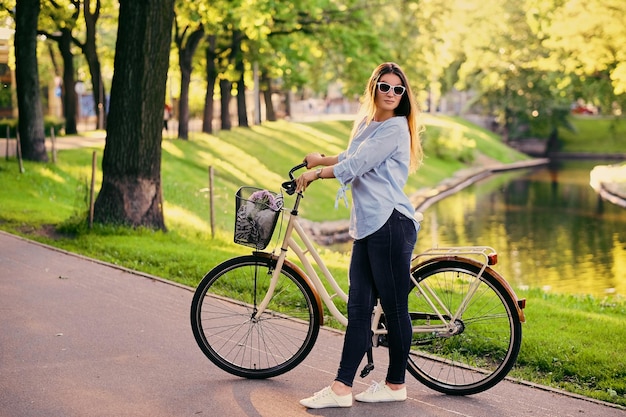 도시 공원에서 자전거를 탄 매력적인 갈색 머리 여성의 초상화.