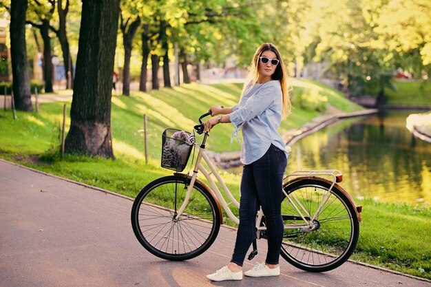 Portrait of an attractive brunette female with a bicycle in the city park.