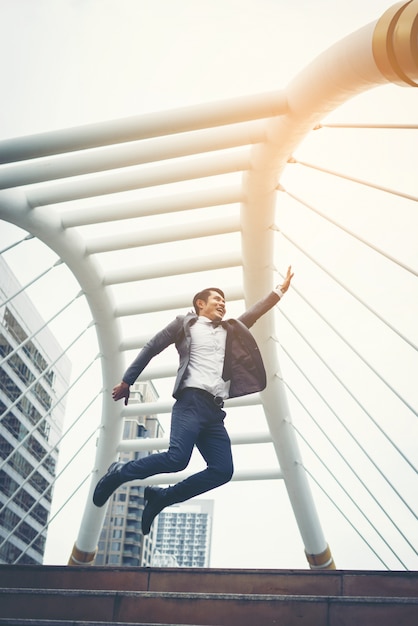 Portrait of Attractive businessman celebrates by jumping raises his fist overhead outdoor.