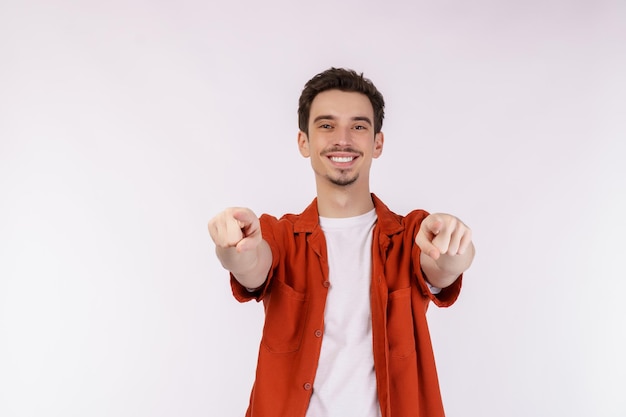 Portrait of attractive cheerful young man pointing finger at camera and standing isolated over background
