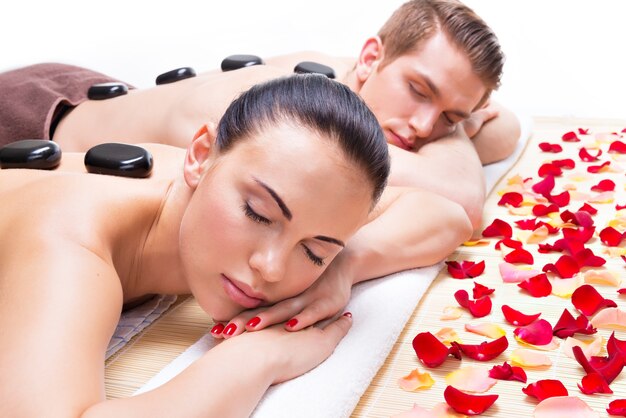 Portrait of attractive couple relaxing in spa salon with hot stones on body.