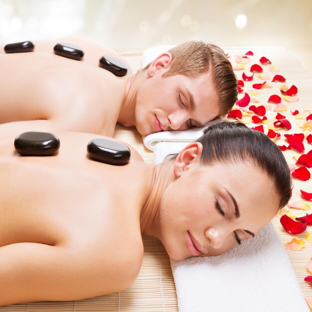 Portrait of attractive couple relaxing in spa salon with hot stones on body.