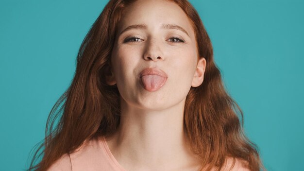 카메라에 혀를 보여주는 매력적인 귀여운 빨간 머리 소녀의 초상화는 유치 한 분위기 표현
