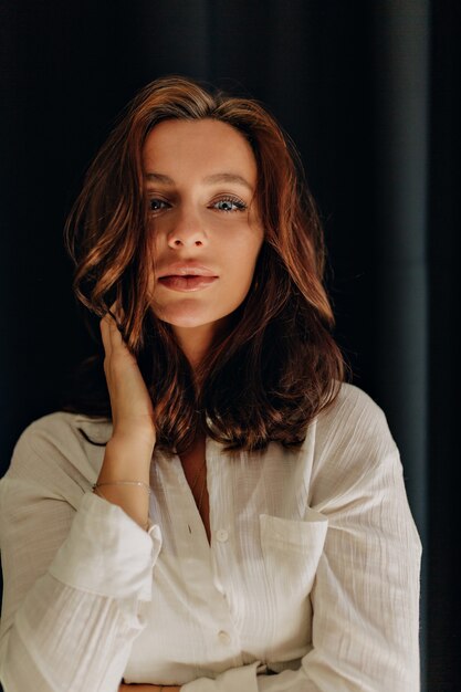 portrait of attractive european woman with dark wavy hair and blue eyes posing touching her face