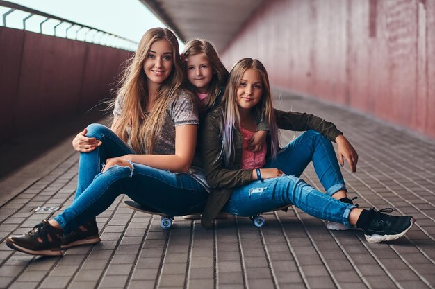 매력적인 가족의 초상화입니다. 다리 보도에서 스케이트 보드에 함께 앉아 어머니와 그녀의 딸.