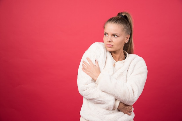 Foto gratuita ritratto di una ragazza attraente che abbraccia se stessa isolato su sfondo rosso