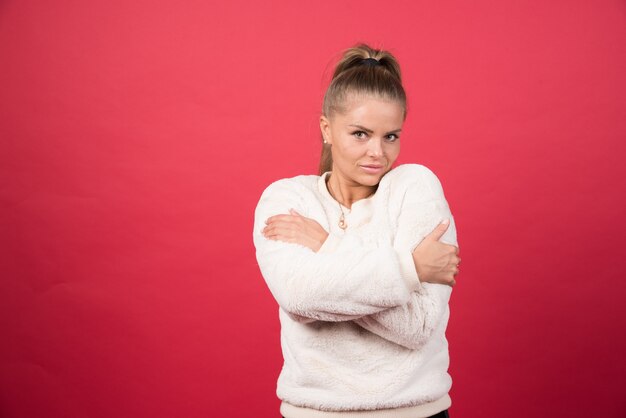 Portrait of an attractive girl hugging herself isolated over red wall