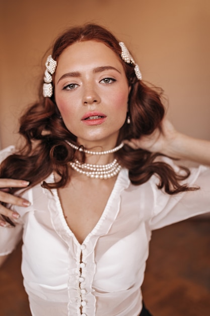 Portrait of attractive green-eyed woman with pearl hairpins on curly hair and beautiful necklace.