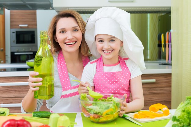 Portrait of attractive happy mother and daughter cooking a salad at the kitchen.