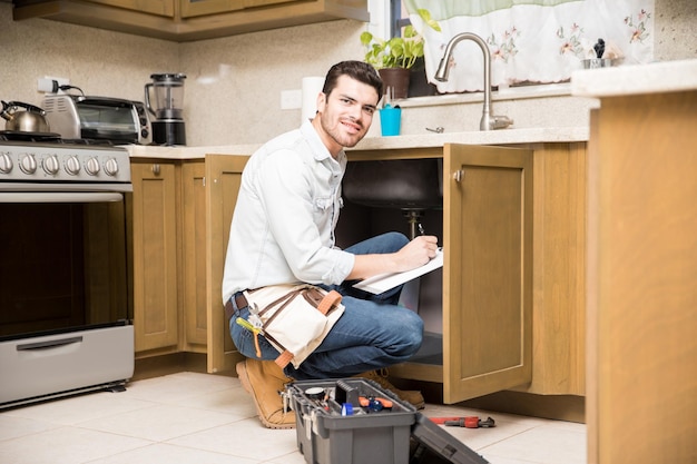 Portrait of an attractive Hispanic handyman writing a work estimate before fixing a kitchen sink