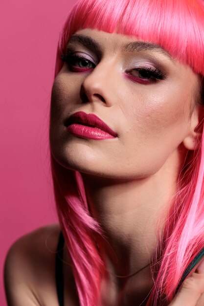 Портрет привлекательной дамы с розовой прической и модным макияжем выглядит уверенно, позируя перед камерой. Беззаботная сексуальная модель с чувственным стилем сидит в фотостудии.