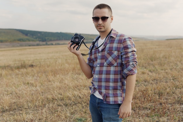 Portrait of attractive male photographer outdoors at sunset. Young man with a camera in hand