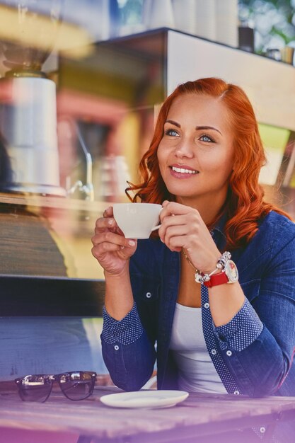 매력적인 빨간 머리 여성의 초상화는 카페에서 커피를 마신다.