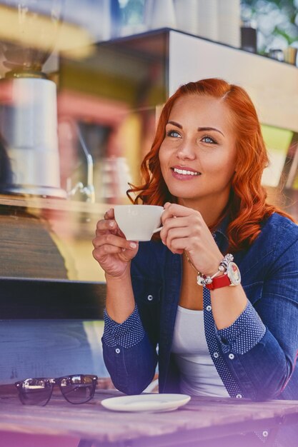 魅力的な赤毛の女性の肖像画は、カフェでコーヒーを飲みます。