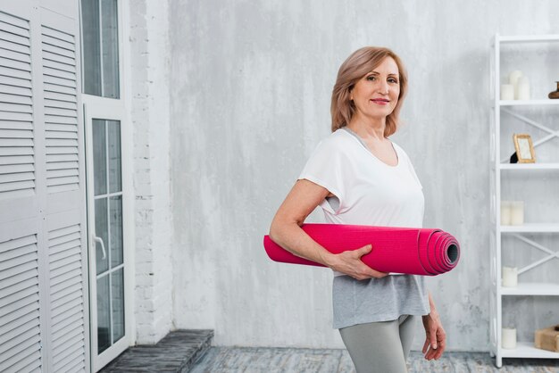 Portrait of a attractive senior woman holding pink mat in hand at home