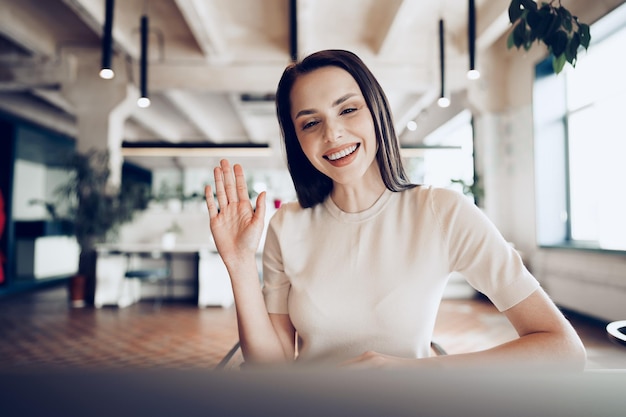 Portrait of attractive smiling businesswoman waving hand looking at camera