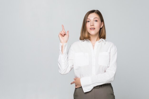 Portrait of attractive smiling woman pointing up isolated on white wall