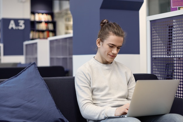 Portrait of attractive student with cute smile relaxing at home with generic laptop computer, messaging online