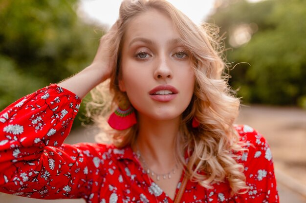 Portrait of attractive stylish blond smiling woman in red blouse summer fashion outfit  wearing earrings smiling