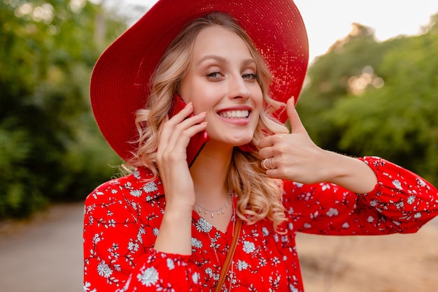 Portrait of attractive stylish blond smiling woman in straw red hat and blouse summer fashion outfit  talking on phone positive gesture emotion