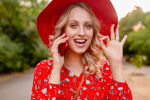 Portrait of attractive stylish blond smiling woman in straw red hat and blouse summer fashion outfit  talking on phone positive gesture emotion