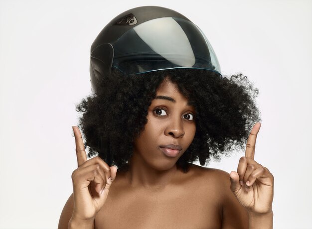 Портрет привлекательной удивленной афро-американской женщины в мотоциклетном шлеме на фоне белой студии. Концепция красоты и защиты кожи
