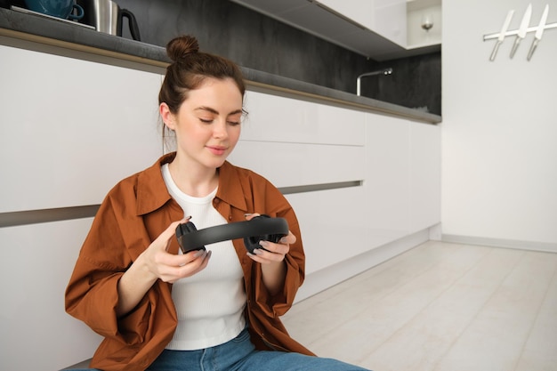 Portrait of attractive woman puts on wireless headphones sits on floor relaxing with favourite songs