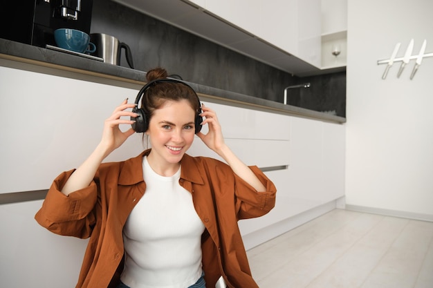 Free photo portrait of attractive woman puts on wireless headphones sits on floor relaxing with favourite songs