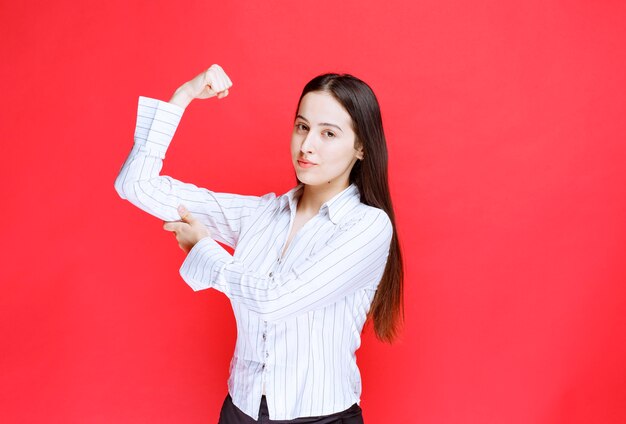 Portrait of attractive woman showing her muscle against red wall. 