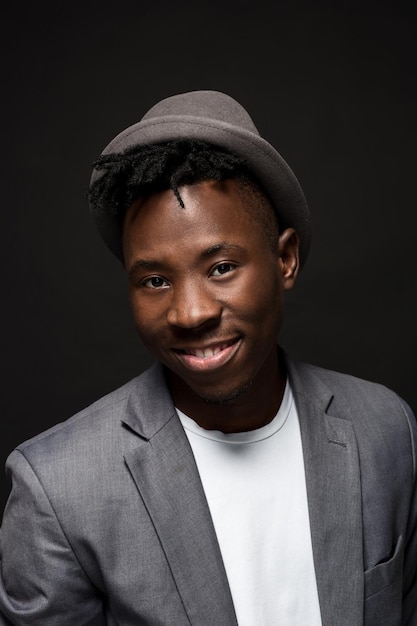 Portrait of attractive young black male studio with hat cheesy smile on dark background