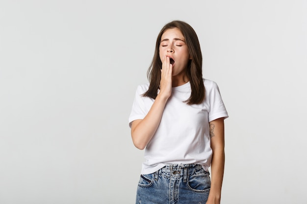 Portrait of attractive young female student yawning tired, feeling sleepy, white