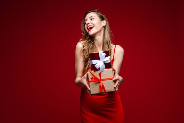 Portrait of attractive young lady in red silk dress holding small wrapped presents
