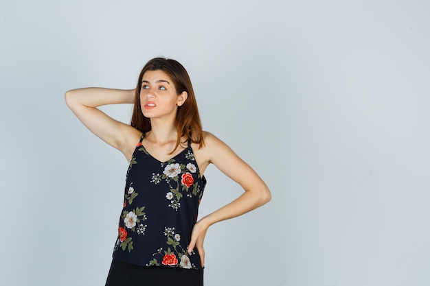 Portrait of attractive young lady scratching head in blouse and looking thoughtful front view