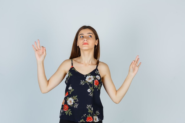 Portrait of attractive young lady showing yoga gesture in blouse and looking hopeful front view