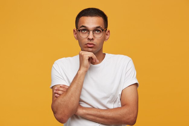 Portrait of attractive young man in glasses looks up ponders a thought or idea