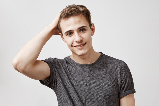 Portrait of an attractive young man in a gray shirt touching his hair.